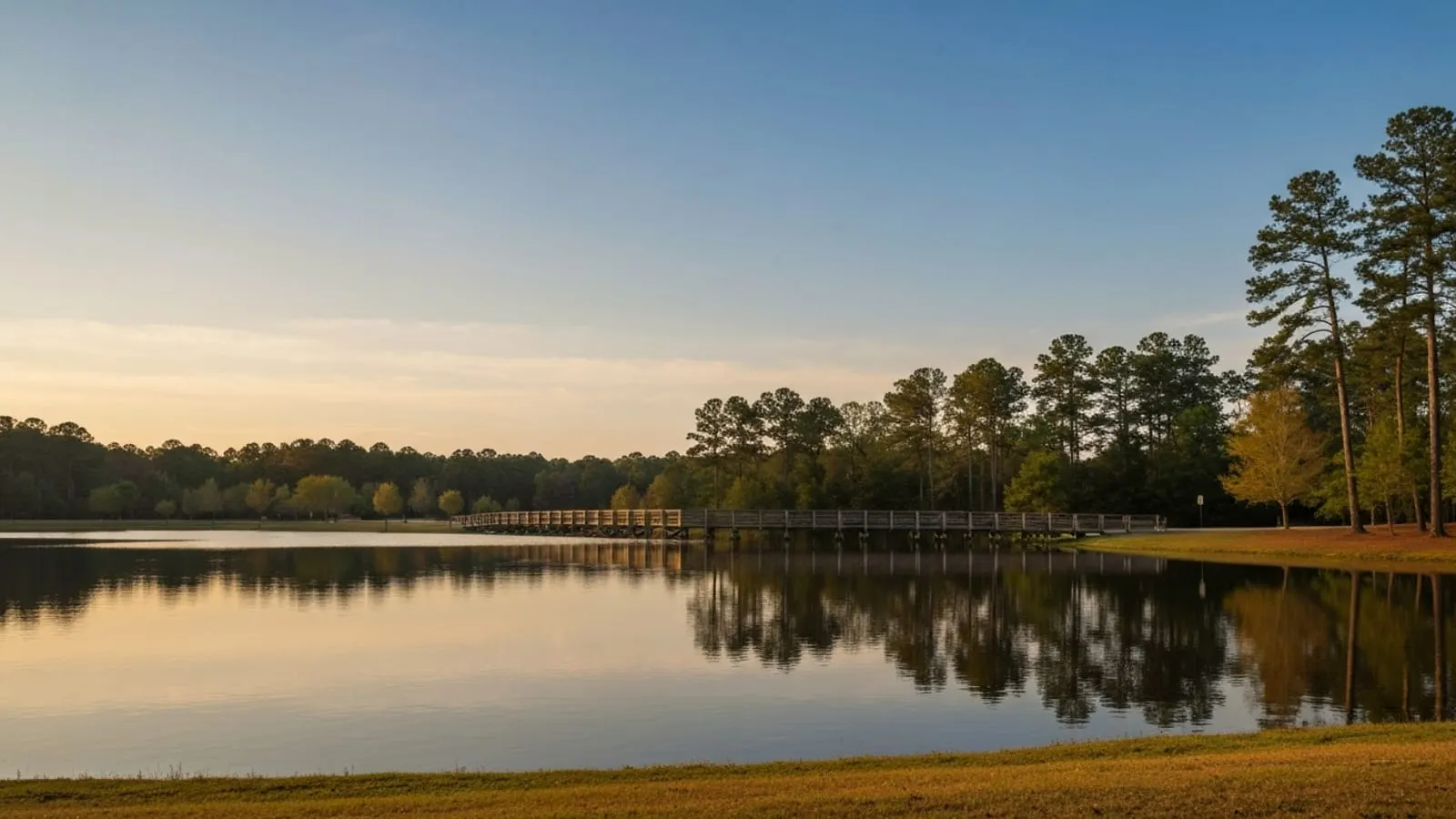Editorial photograph of Fred G. Bond Metro Park in Cary North Carolina at golden hour with the lake reflecting the late afternoon sky and surrounding pine forest.