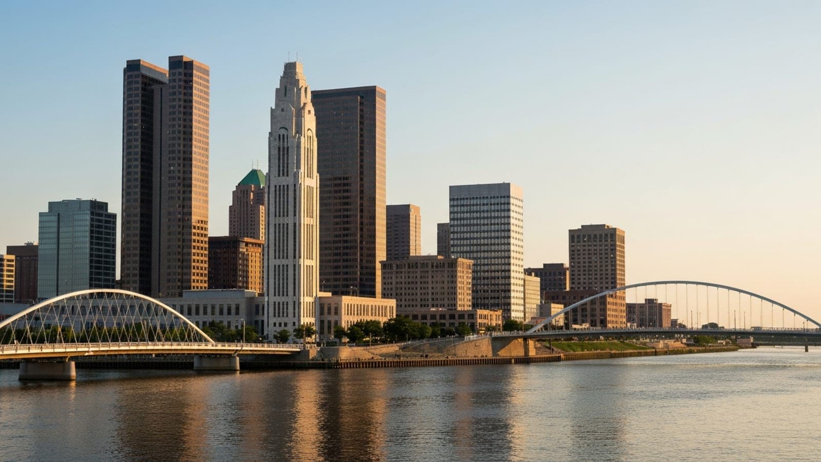 Editorial photograph of the Columbus, Ohio skyline at golden hour with the Scioto River and Scioto Mile waterfront in the foreground, evoking the geography of the Ohio capital.