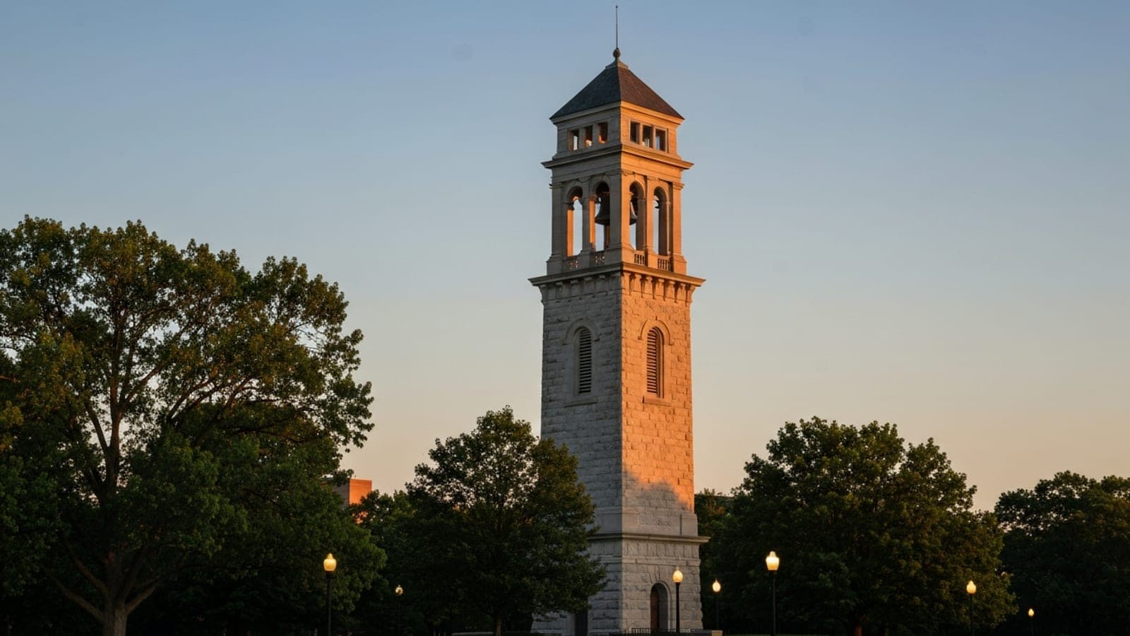 Editorial photograph of the Dayton, Ohio skyline at golden hour with the historic Carillon Park bell tower in the background, evoking the Wright Brothers' aviation heritage and Miami Valley geography.