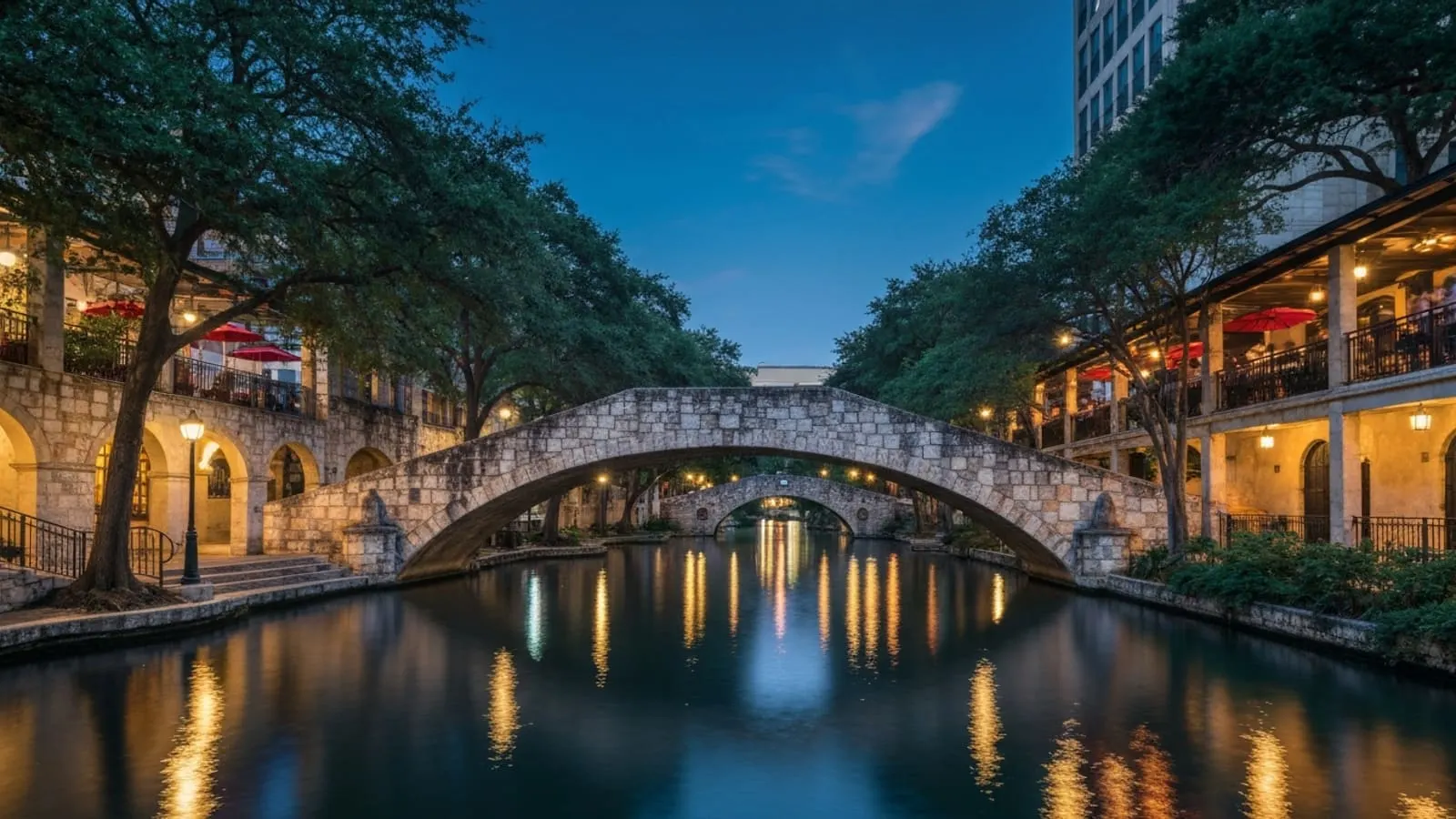 San Antonio River Walk at twilight with stone arch bridges and cypress trees reflecting in the water