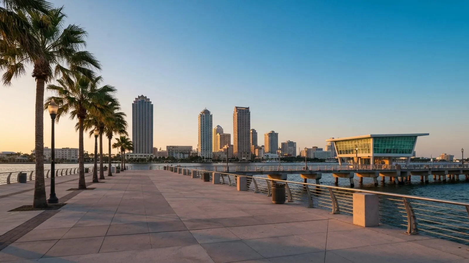Editorial photograph of the St. Petersburg Pier District at golden hour with a waterfront pier extending into Tampa Bay and the downtown skyline behind.